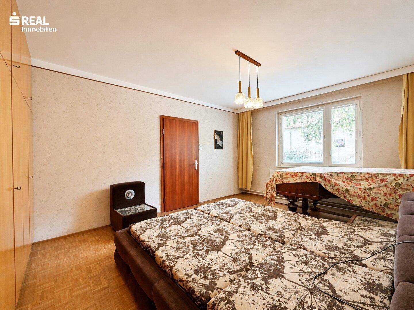 Schlafzimmer mit Doppelbett, Holzschrank und gemustertem Bodenbelag.