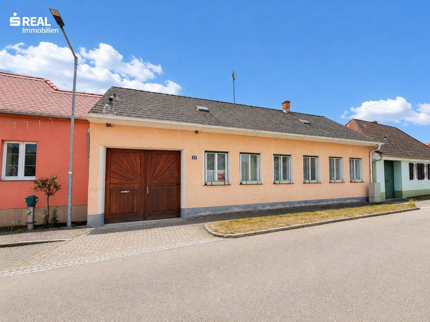 Fassade eines traditionellen Gebäudes mit Holztor und mehreren Fenstern zur Straße hin.