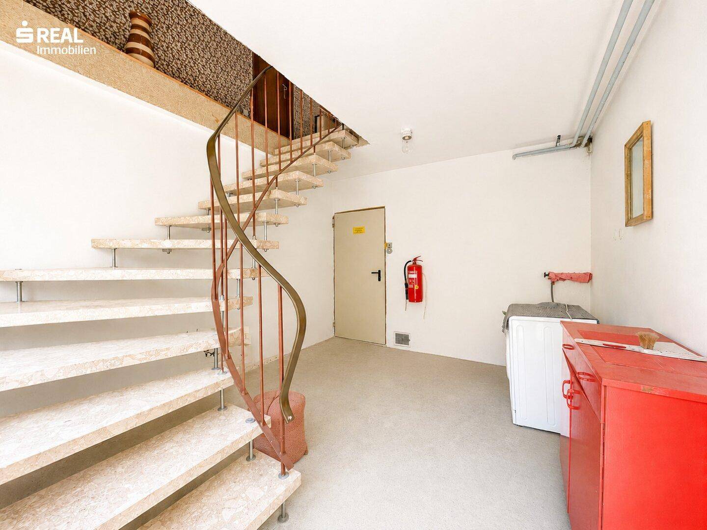 Treppenhaus mit geschwungener Steintreppe und weiß gestrichenen Wänden.