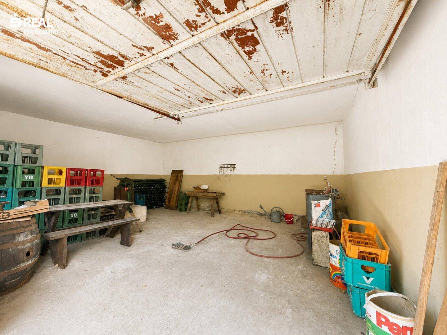 Geräumiger Lagerraum mit Betonboden, weiß getünchten Wänden und einer rustikalen Holzdecke.