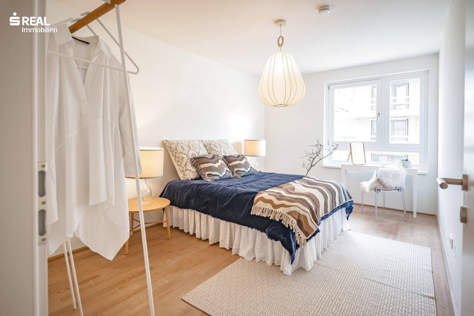 Helles Schlafzimmer mit Holzboden, großem Fenster und modernem Kleiderständer.