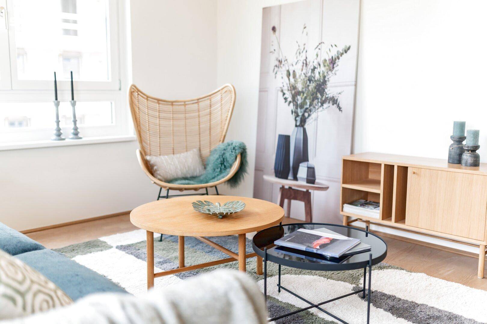 Detailansicht des Wohnzimmers mit Rattan-Sessel, Couchtischen und dekorativen Elementen.