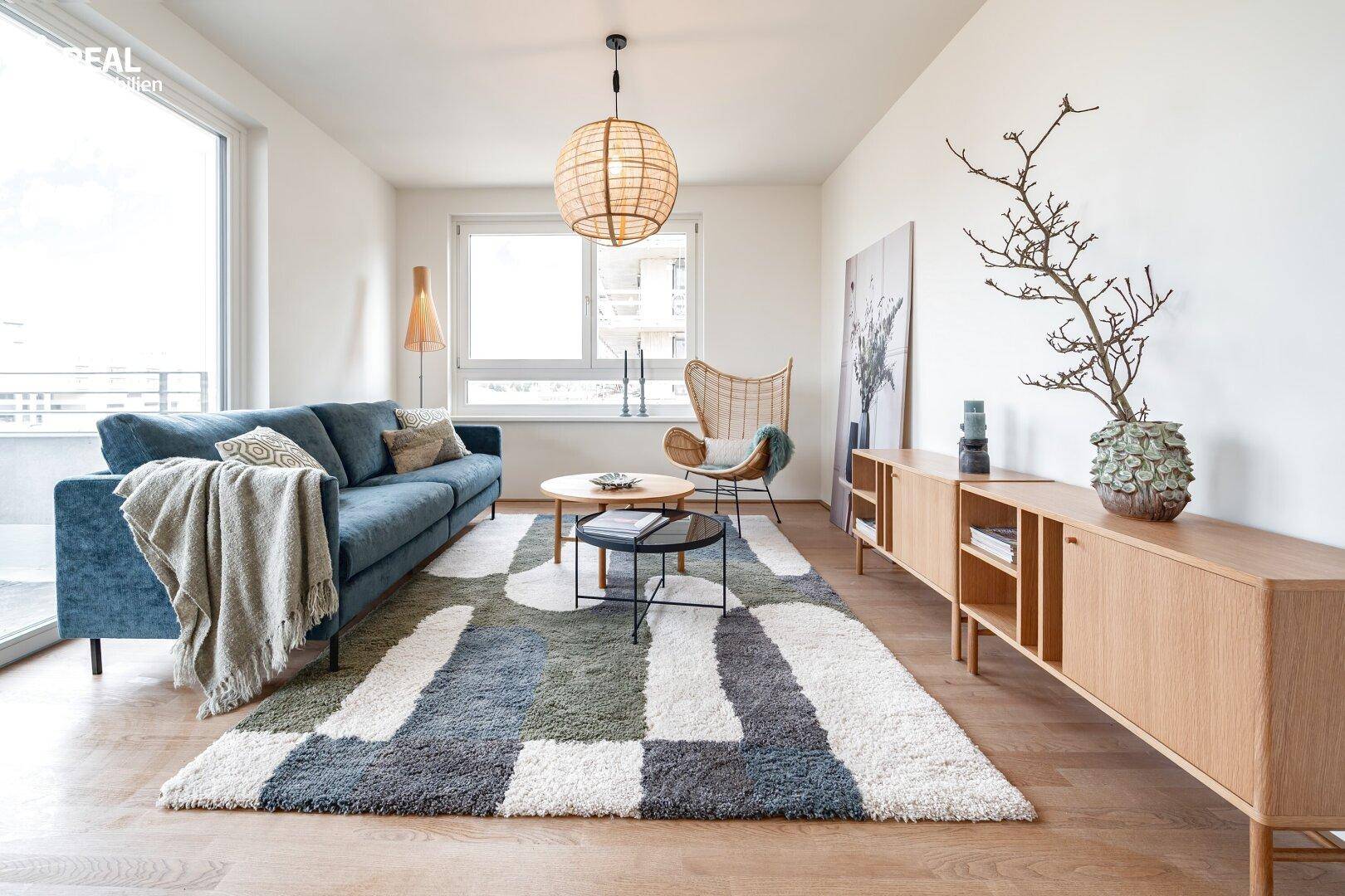 Helles Wohnzimmer mit Sofa, Rattansessel und dekorativem Teppich, einladend und modern eingerichtet.