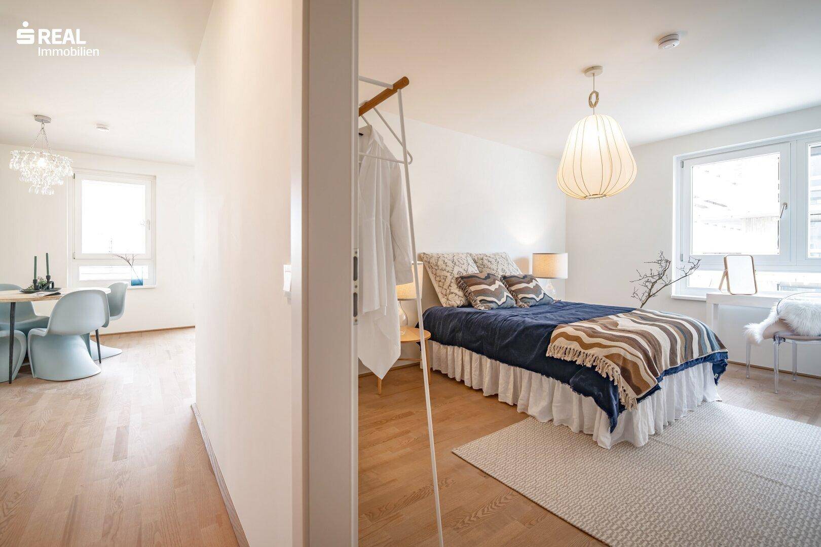 Schlafzimmer mit Doppelbett und Blick in den angrenzenden Essbereich, offen und hell gestaltet.
