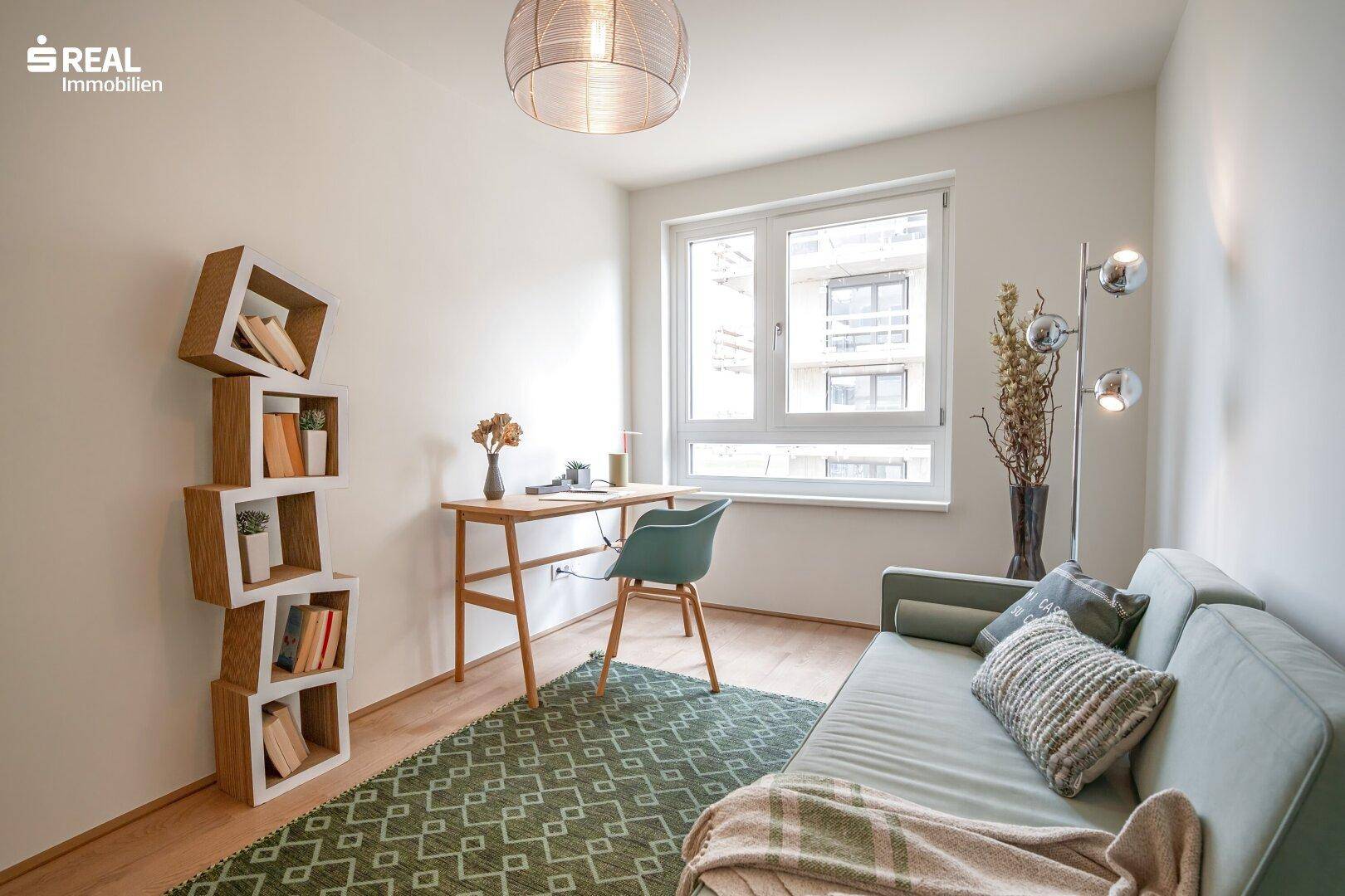 Helles Arbeitszimmer mit Schreibtisch, Sofa und dekorativem Regal.