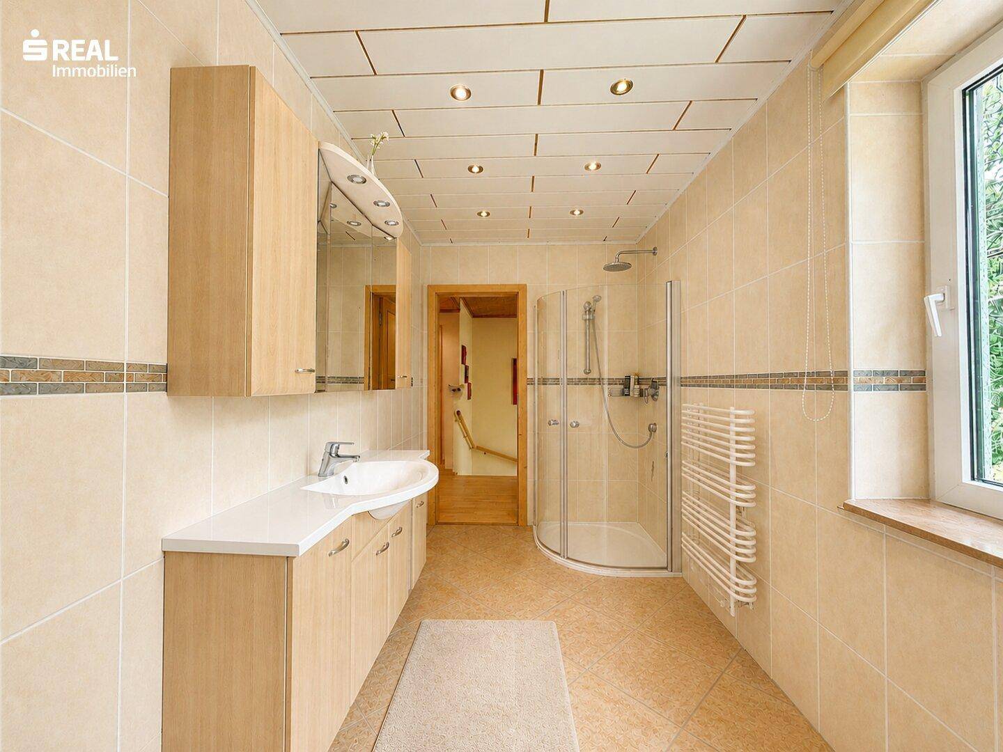 Modernes Badezimmer mit beigefarbenen Fliesen, Duschkabine und beheiztem Handtuchhalter.