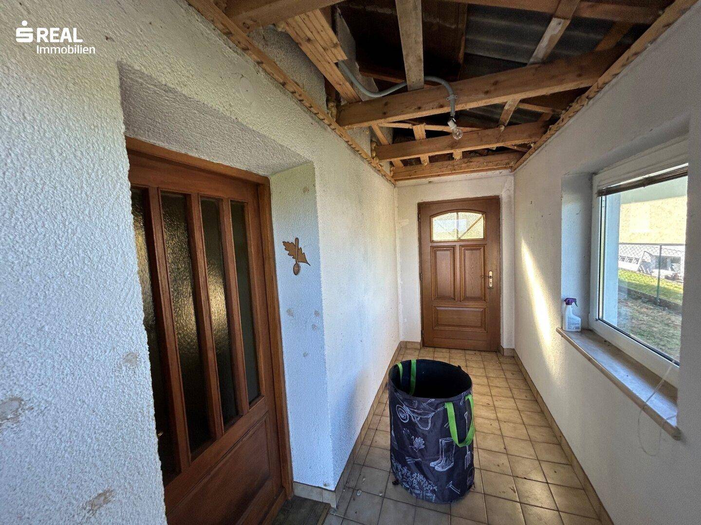 Eingangsbereich mit zwei Holztüren, Fliesenboden und sichtbarer Deckenkonstruktion.