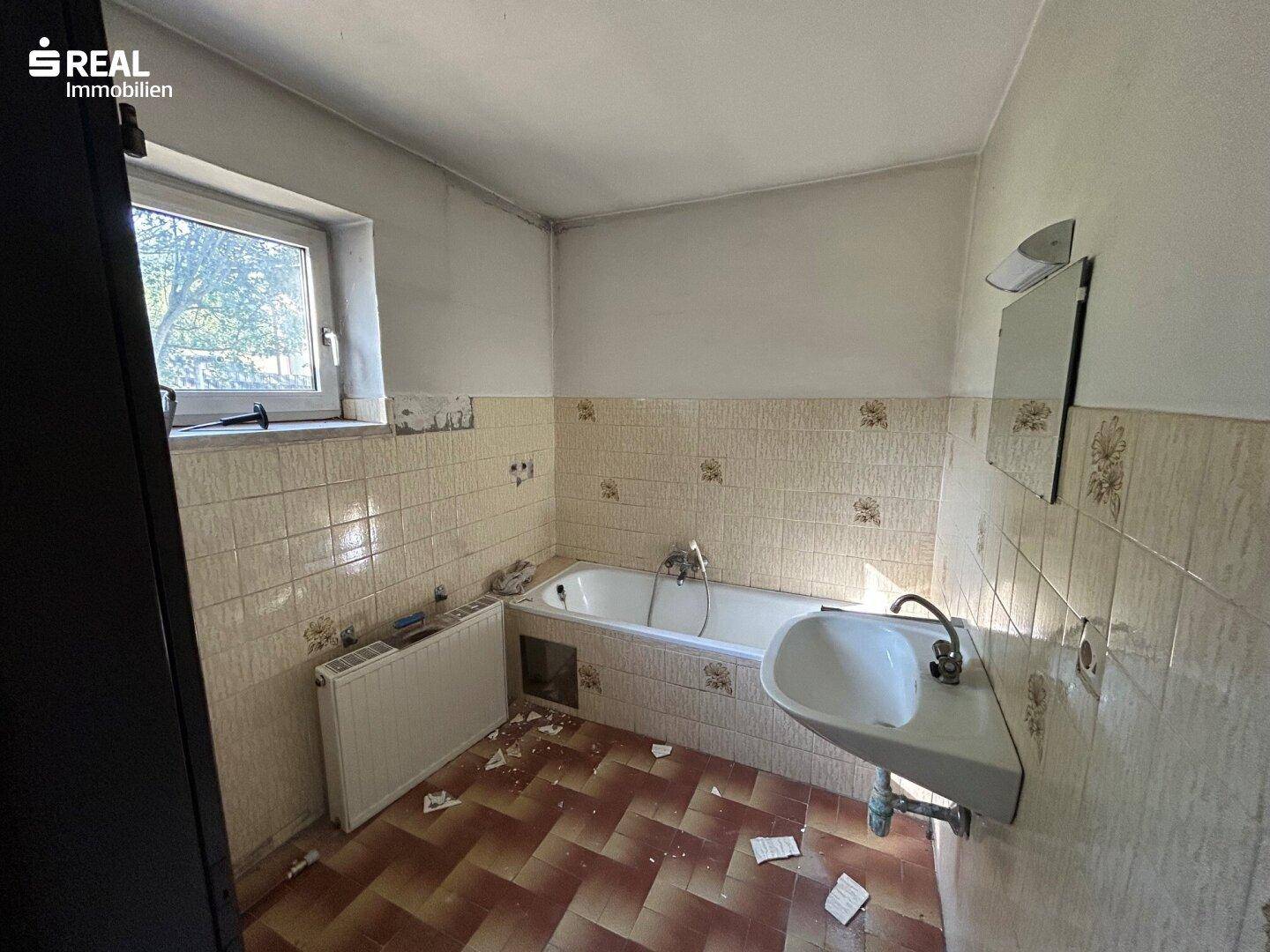 Badezimmer in Renovierung mit Badewanne, Waschbecken und Fliesen im 80er-Jahre-Stil.