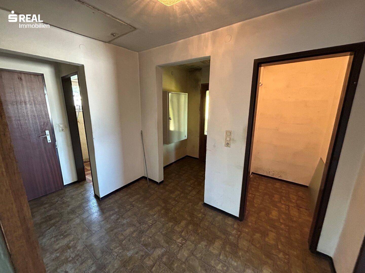 Flur mit mehreren Türen und älterem Bodenbelag, der auf Renovierung wartet.