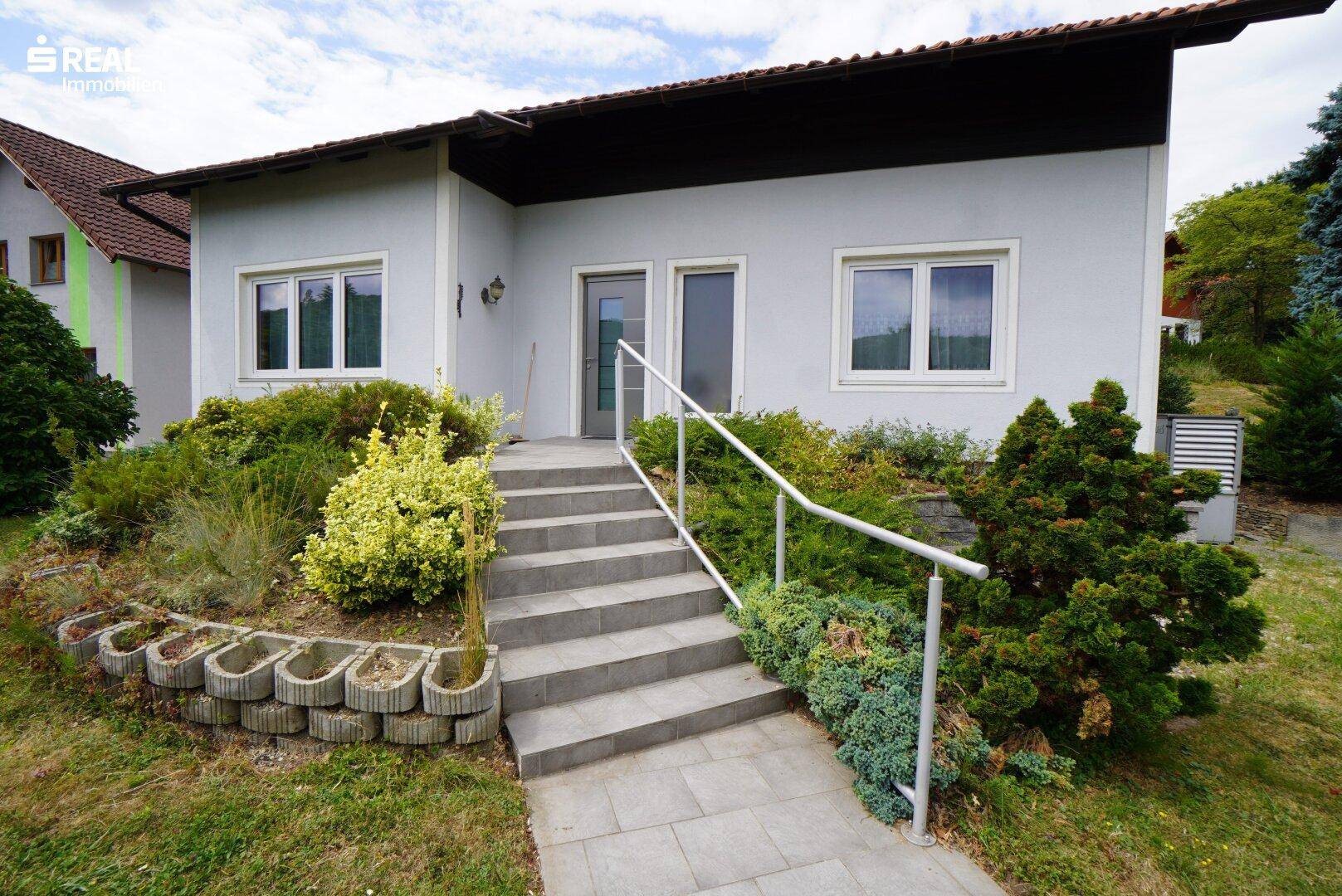 Eingangsbereich des Hauses mit Treppe, Geländer und gepflegter Bepflanzung.