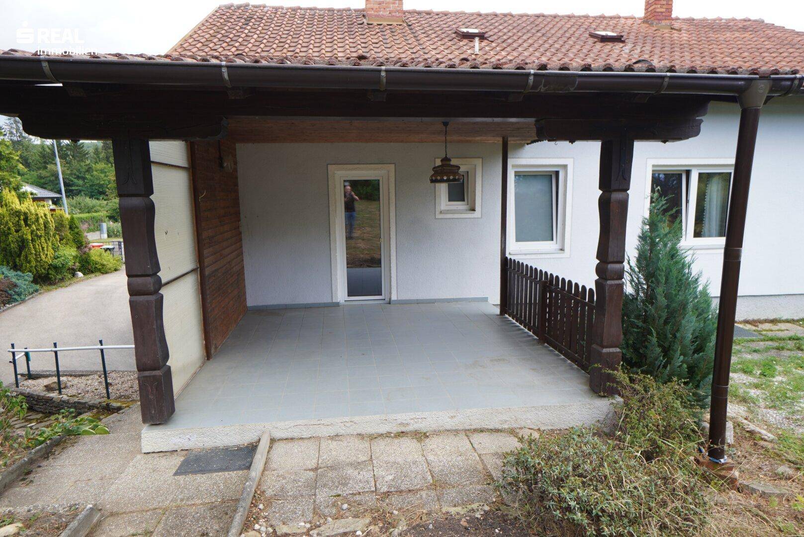 Geräumige überdachte Terrasse mit Holzbalken und Zugang zum Haus.