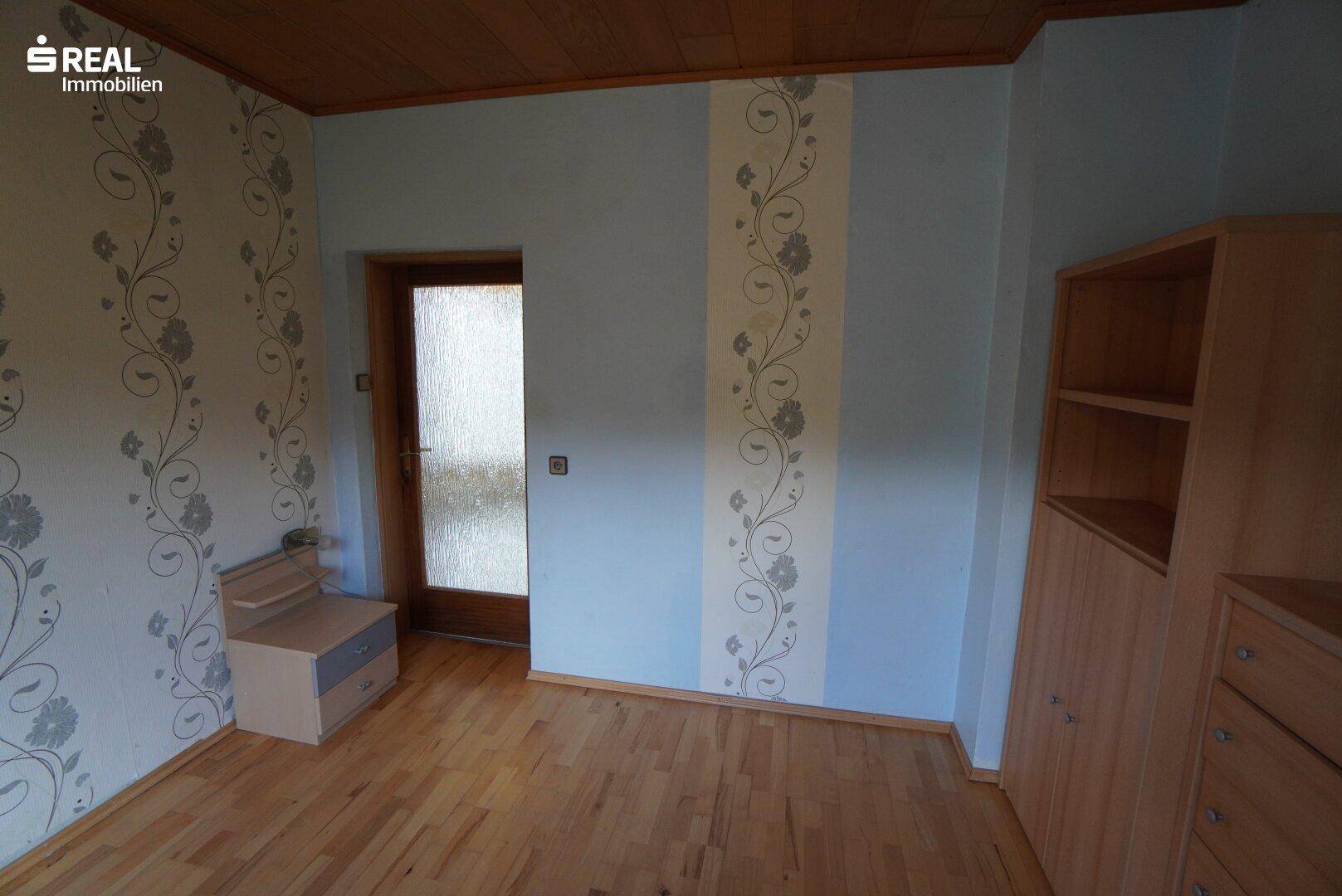 Schlafzimmer mit Parkettboden, Holzdecke und floraler Tapete, bereit zur individuellen Gestaltung.