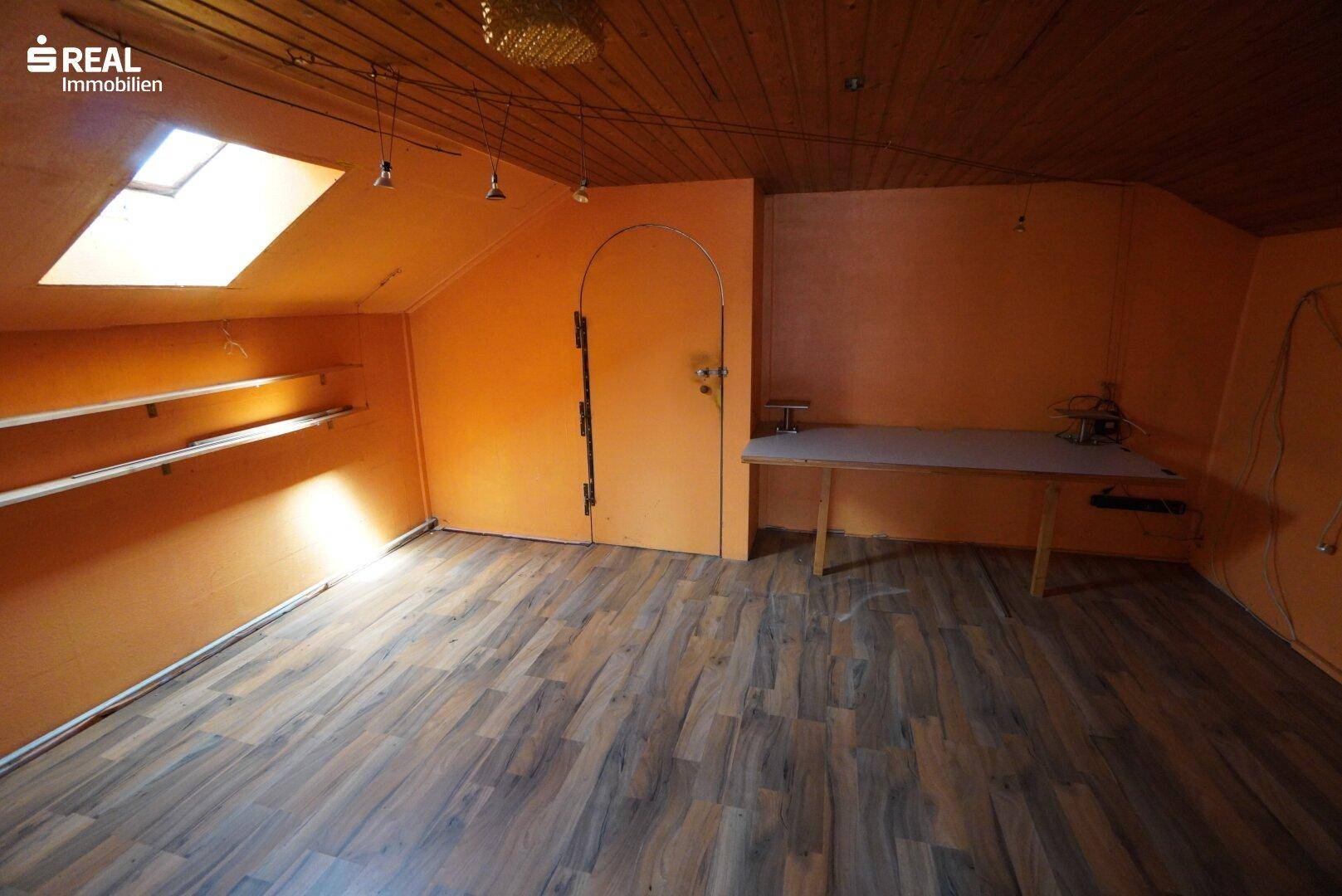 Ausgebauter Dachboden mit Holzboden, orangefarbenen Wänden und einem hellen Dachfenster.