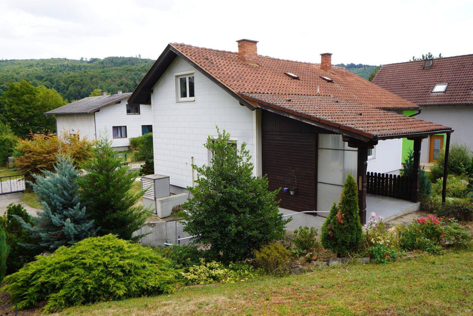 Rückansicht des Hauses mit überdachtem Bereich und gepflegtem Garten in Hanglage.