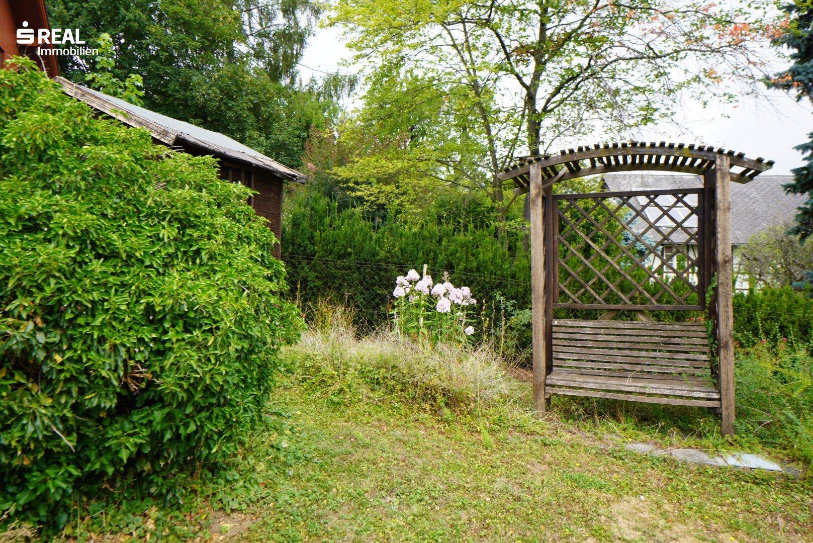 Ruhiger Gartenbereich mit einer hölzernen Gartenbank und blühenden Pflanzen.
