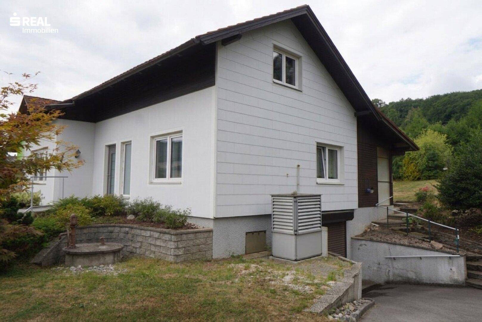 Einfamilienhaus mit weißer Fassade, Satteldach und umgebender Grünfläche in ländlicher Umgebung.