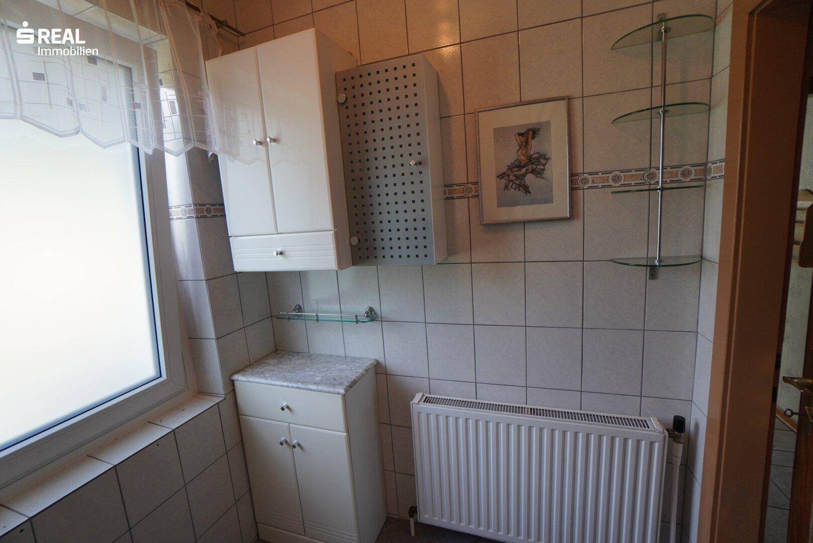 Helles Badezimmer mit Fenster, Heizkörper und praktischen Ablagemöglichkeiten.