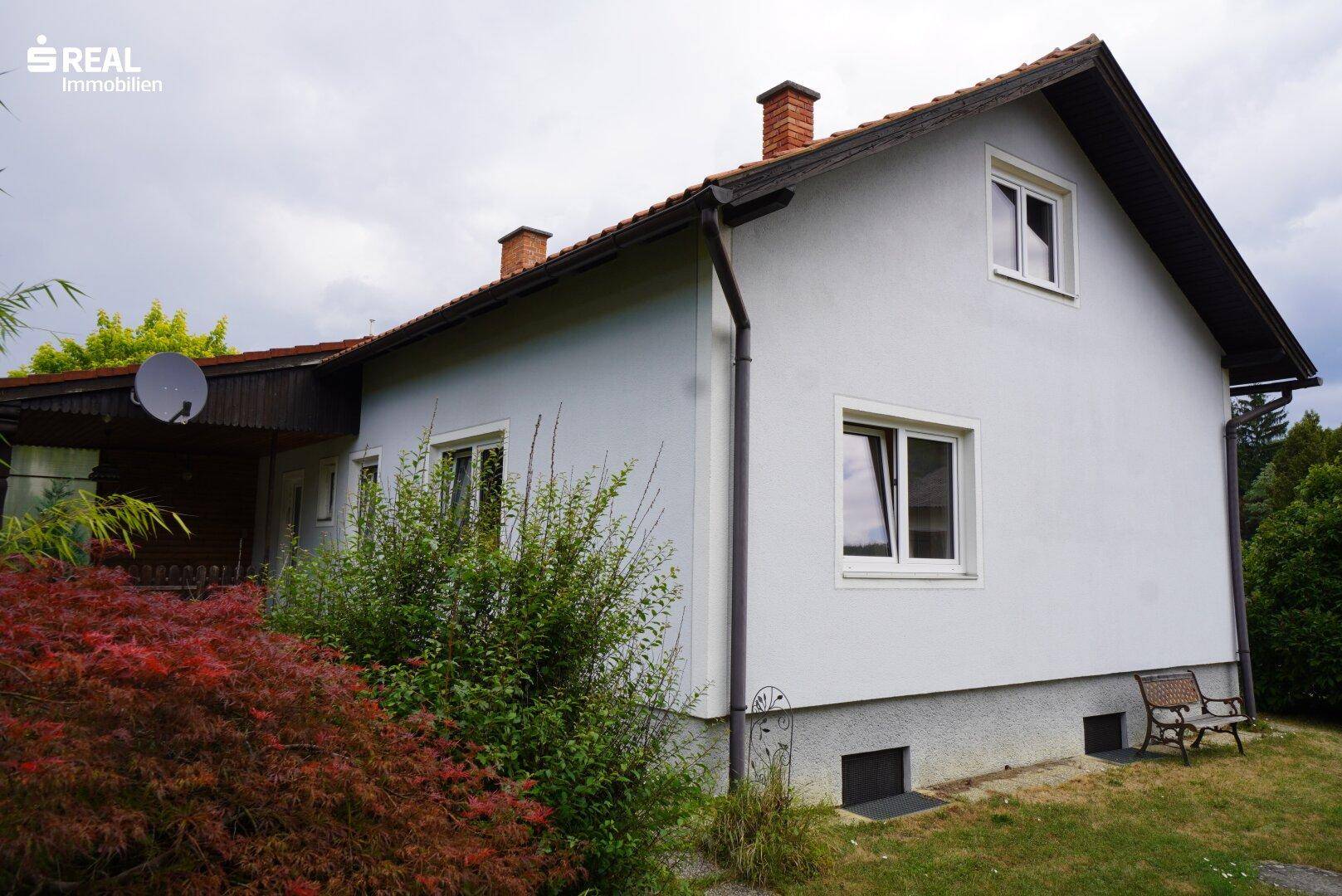 Rückansicht des Hauses mit Dach und Schornsteinen, umgeben von grüner Vegetation.