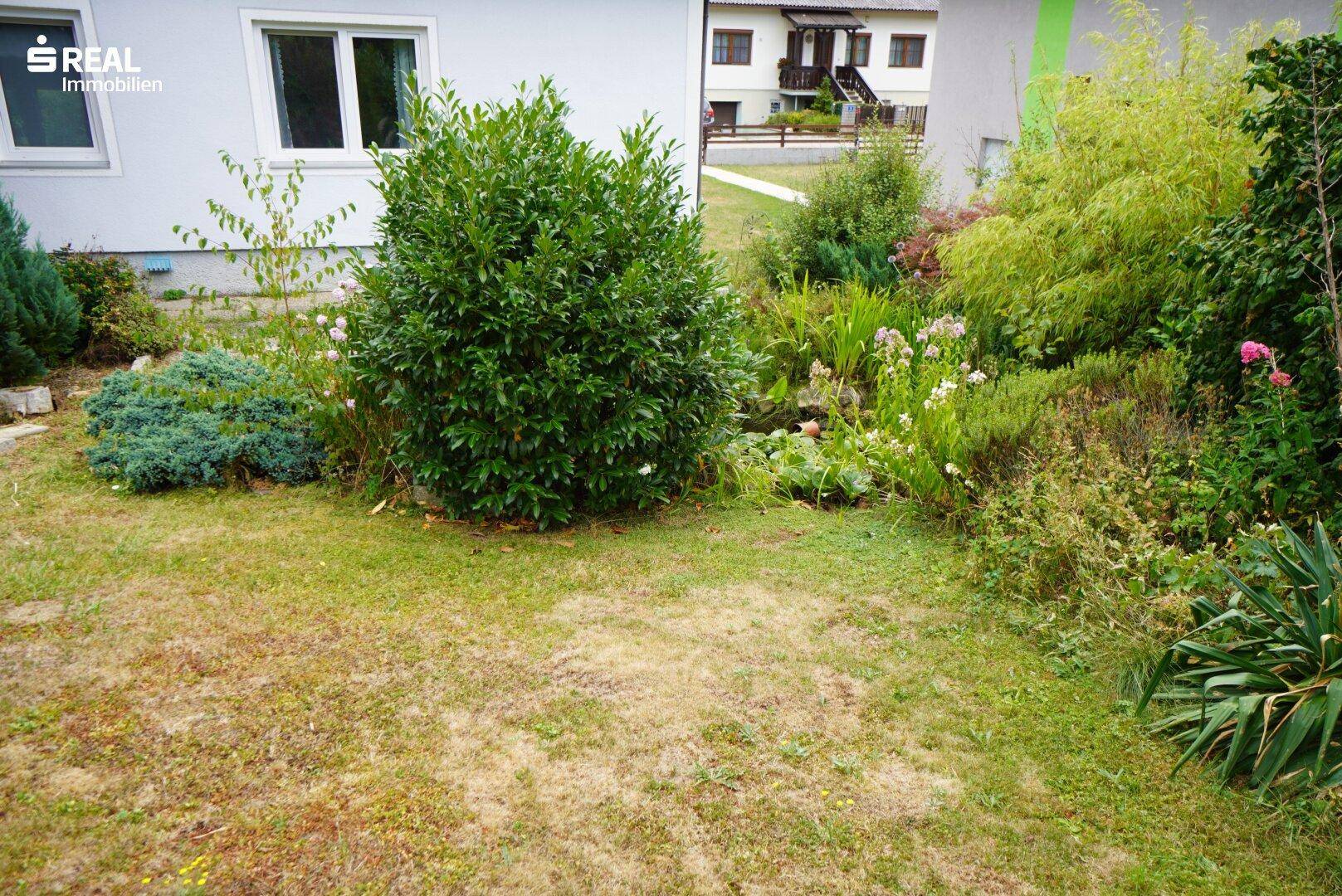Gepflegter Garten mit Rasenfläche, Sträuchern und Blumenbeeten neben dem Haus.