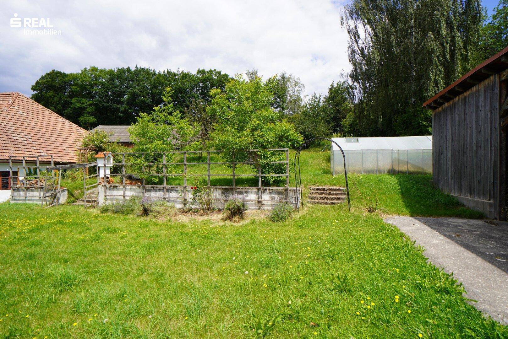 Weitläufiger Garten mit Rasenflächen, Hochbeeten, Gewächshaus und einem Unterstand.