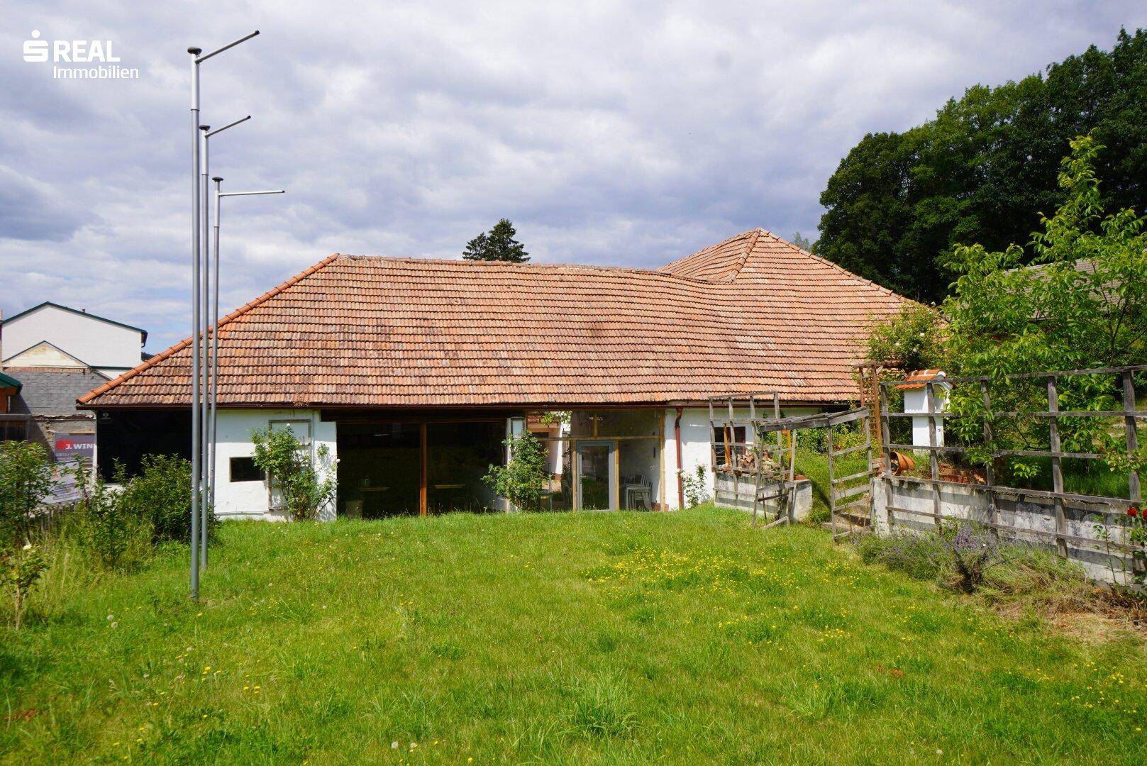 Ländliches Gebäude mit Ziegeldach und großem Garten, umgeben von Bäumen und Natur.