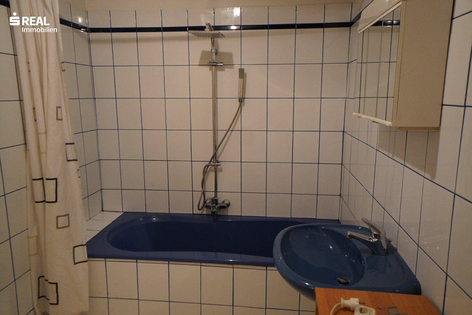 Badezimmer mit blauer Badewanne, passendem Waschbecken und weiß-blau gefliesten Wänden.