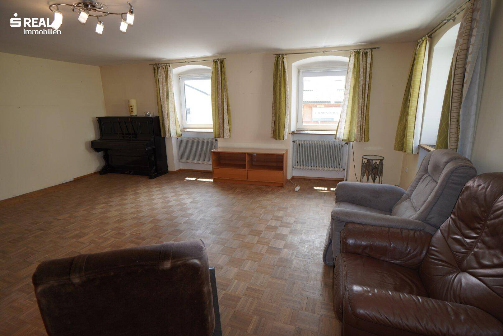 Weiterer Blick ins Wohnzimmer mit Klavier, bequemen Sesseln und klassischem Parkettboden.