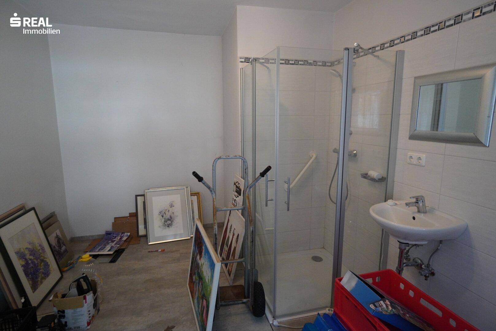 Badezimmer mit Glasduschkabine, Waschbecken und weißen Fliesen, derzeit als Abstellraum genutzt.