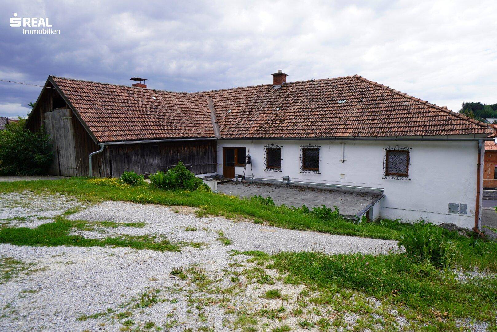 Rückansicht eines Gebäudes mit großer Terrasse und angrenzender Grünfläche unter bewölktem Himmel.