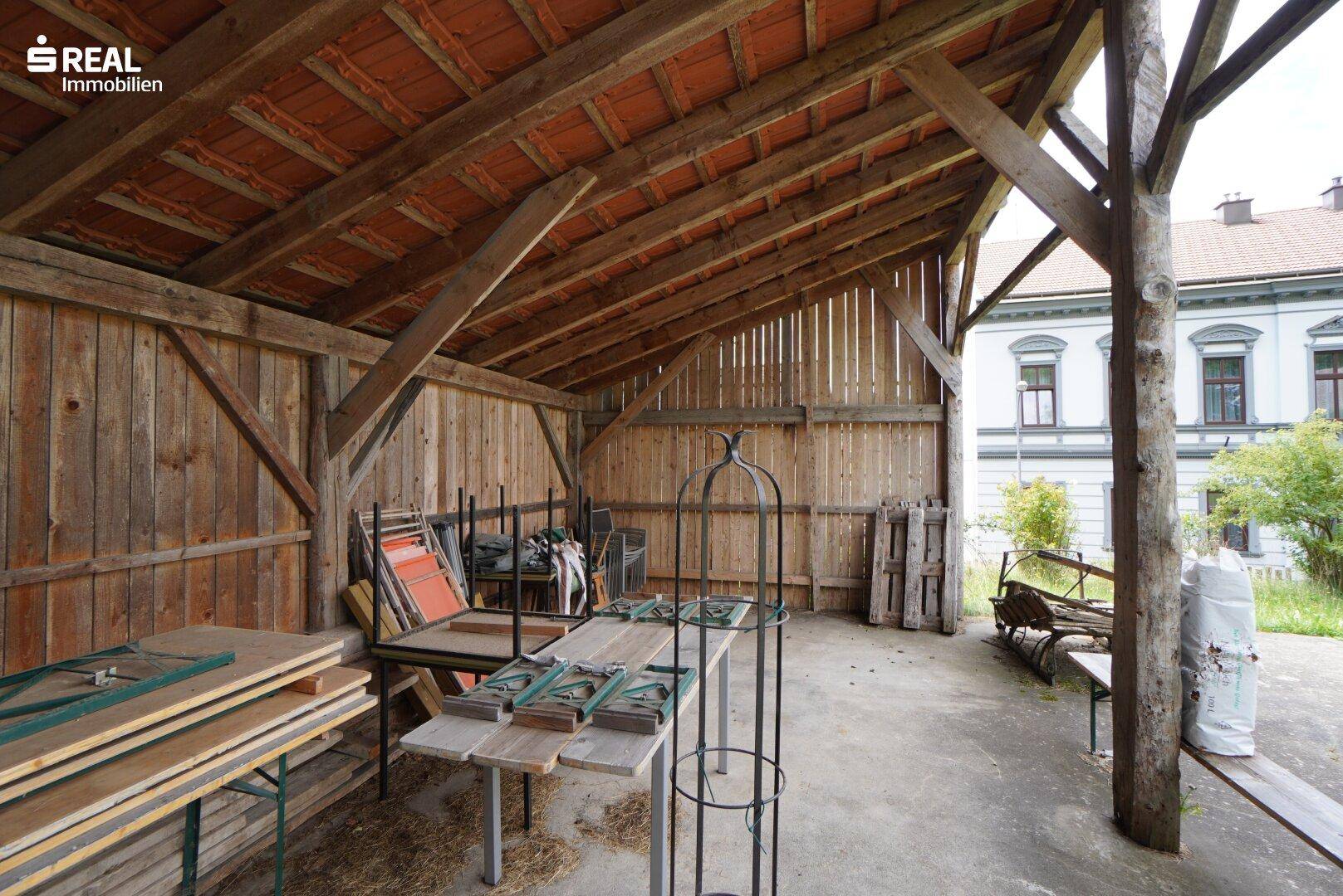 Innenansicht eines offenen Holzunterstands mit sichtbaren Dachbalken und Ziegeln.