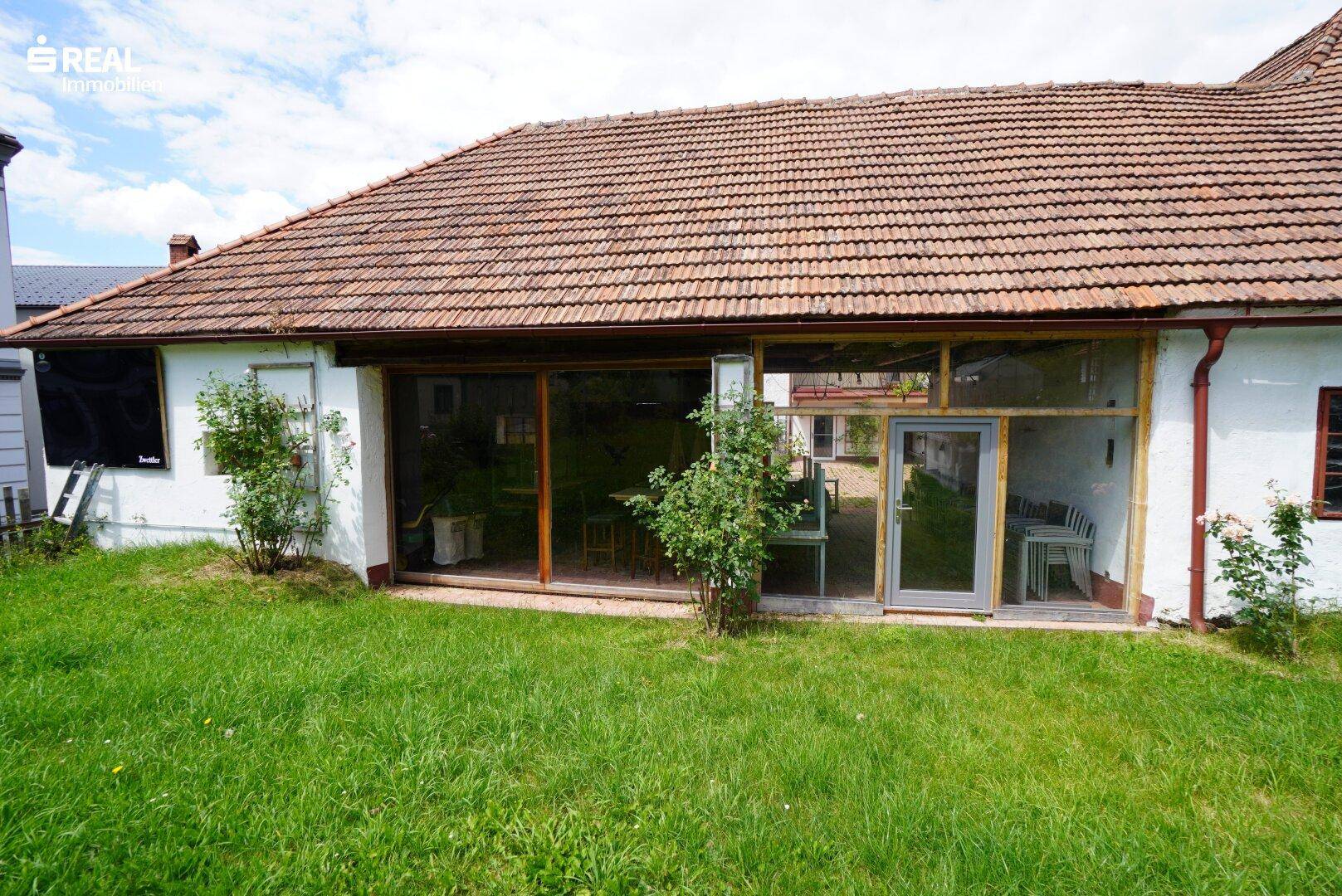 Gebäude mit großen Fenstern und Zugang zum grünen Garten, umgeben von üppiger Vegetation.
