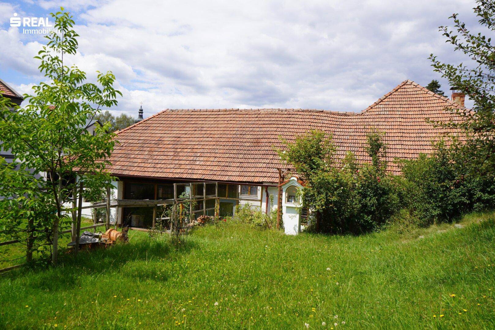 Rückseite eines ländlichen Gebäudes mit Ziegeldach und einem weitläufigen, grünen Gartenbereich.