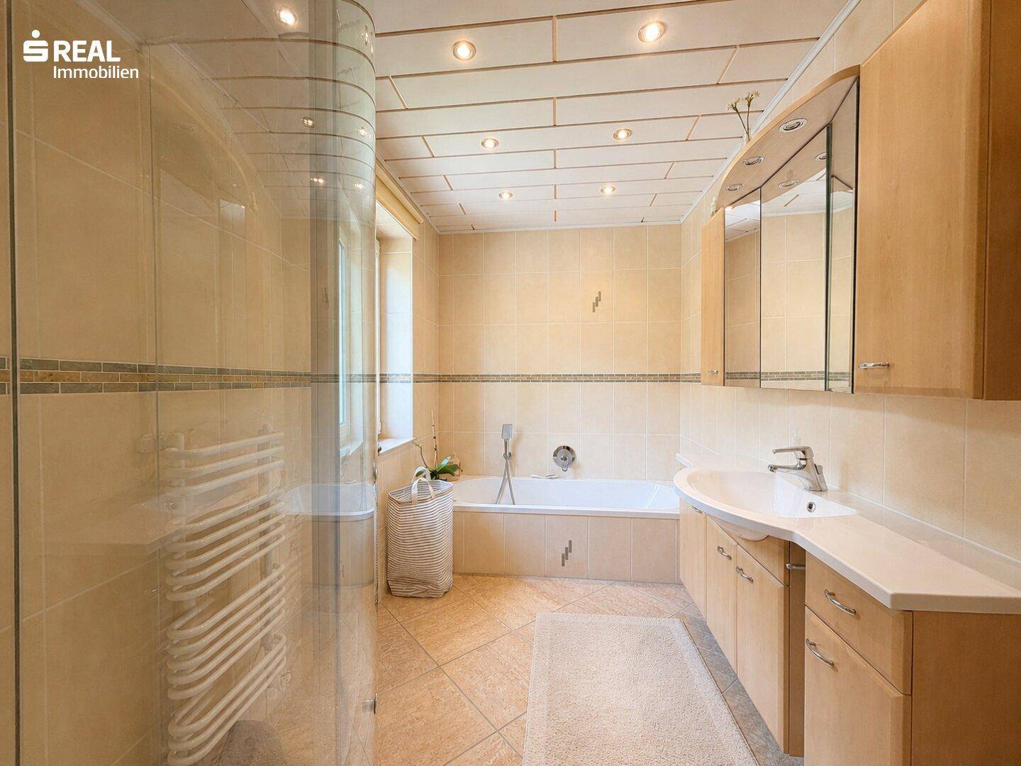 Helles Badezimmer mit beigefarbenen Fliesen, Badewanne, Duschkabine und beheiztem Handtuchhalter.