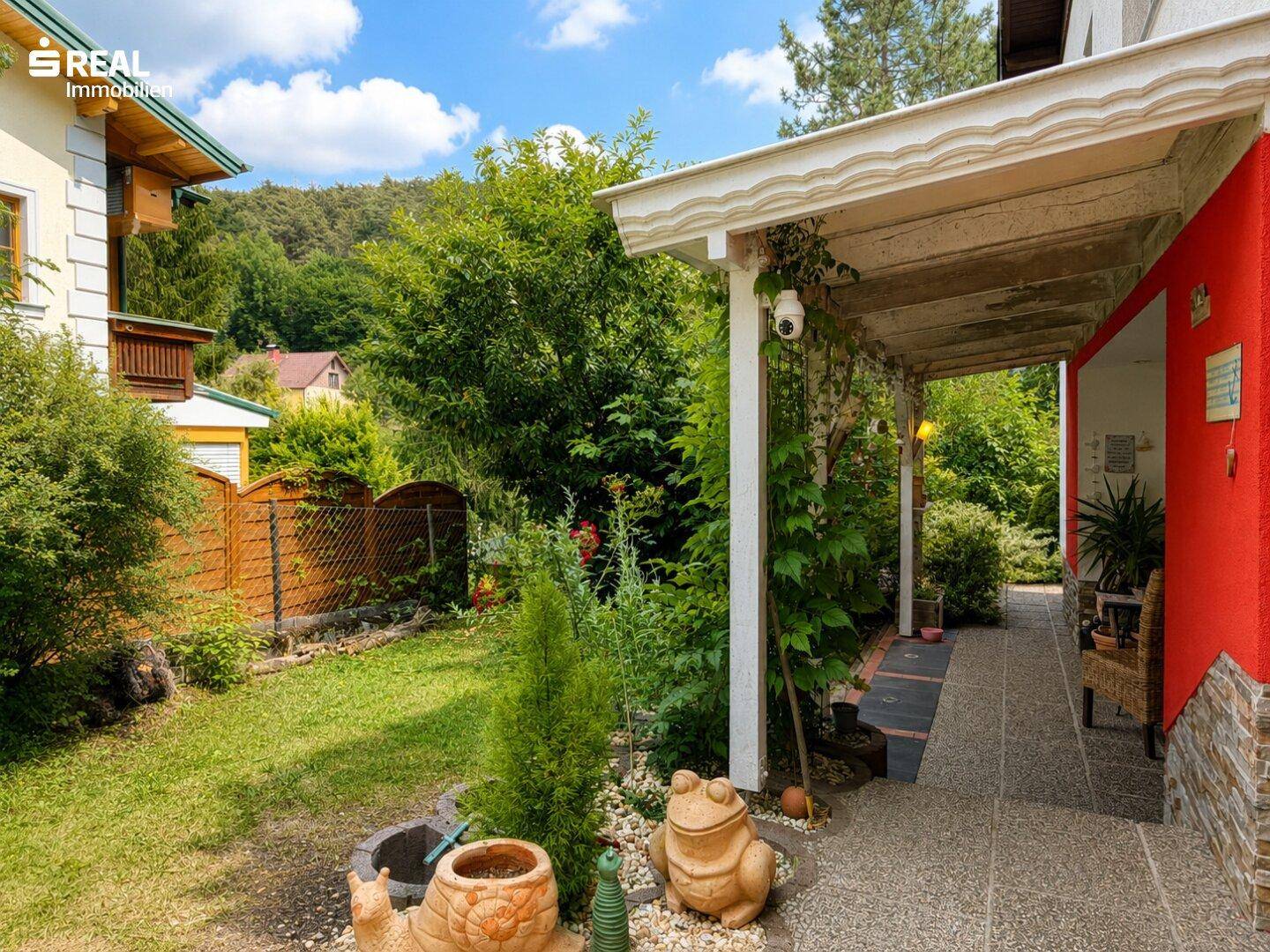Überdachter Gang entlang des Hauses mit Zugang zum Garten und verspielten Gartenzwergen.