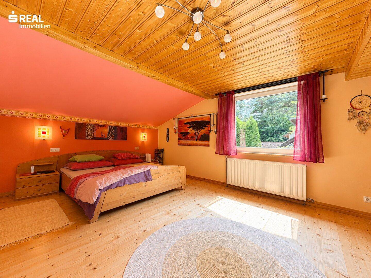 Farbiges Schlafzimmer im Dachgeschoss mit Holzdecke, Holzboden und großem Fenster.