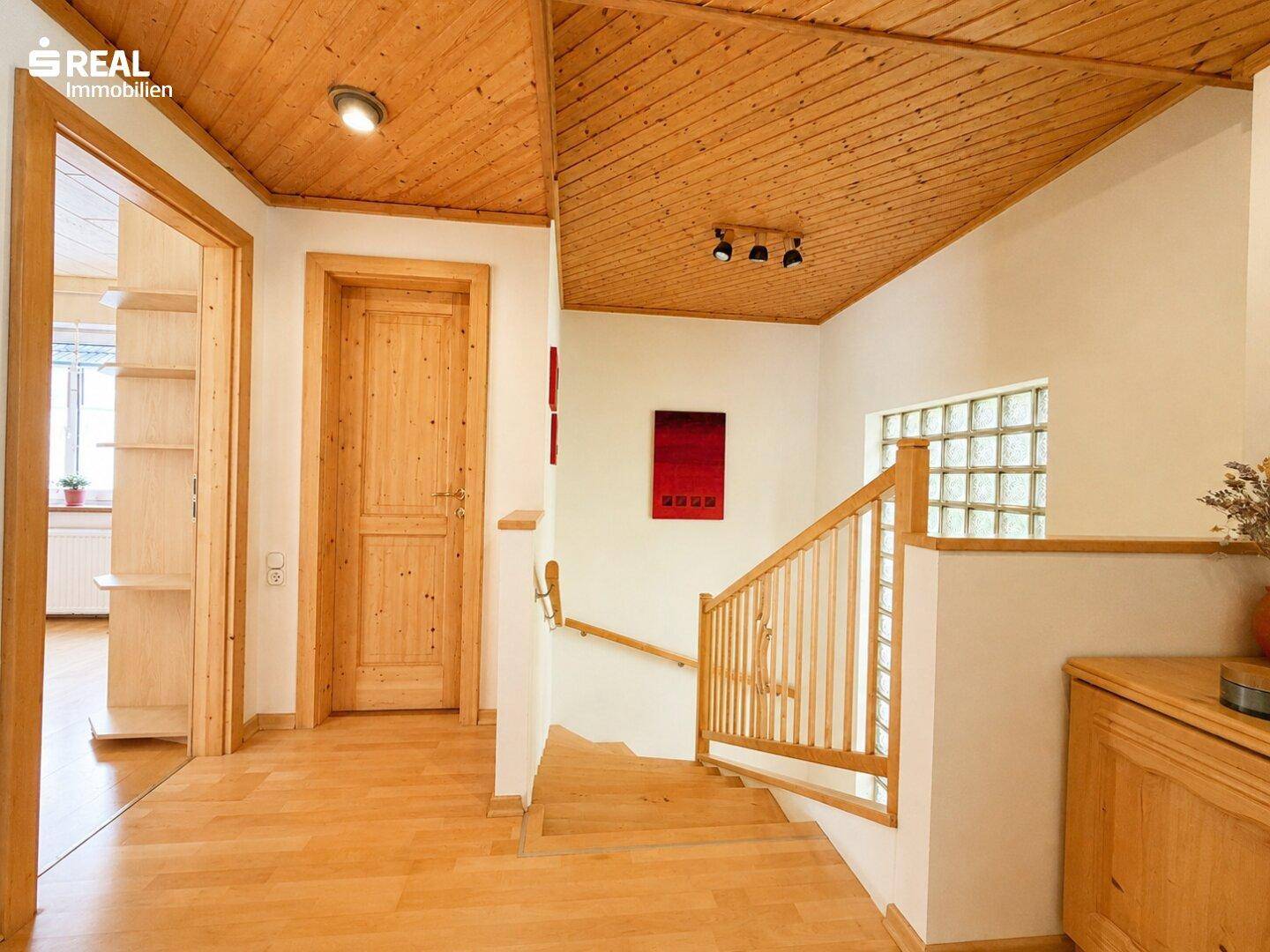 Heller Flur mit Holztreppe, Holzdecke und einem dekorativen Glasbausteinfenster.