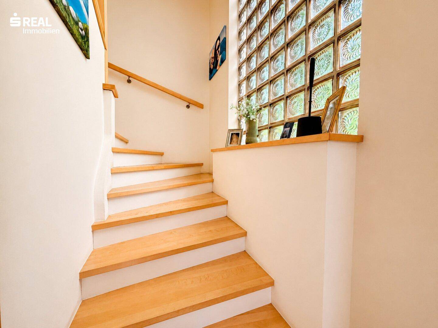 Holztreppe mit weiß gestrichenen Wänden und einem dekorativen Glasbausteinfenster.