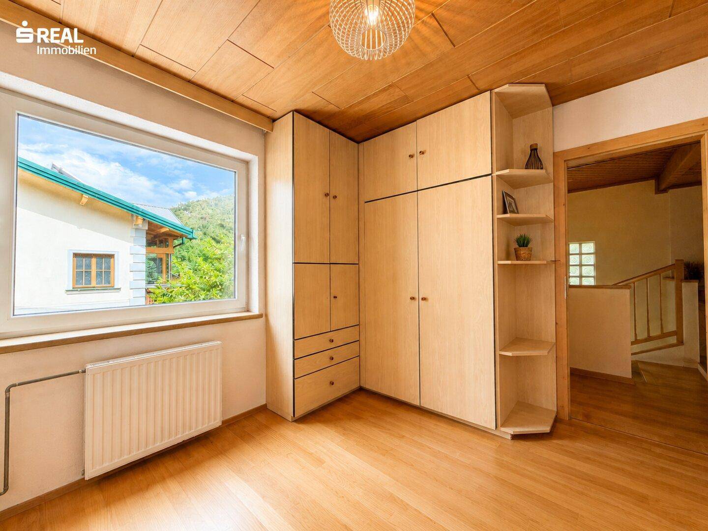 Helles Zimmer mit Einbauschränken, Holzboden und einem Fenster mit Blick nach draußen.