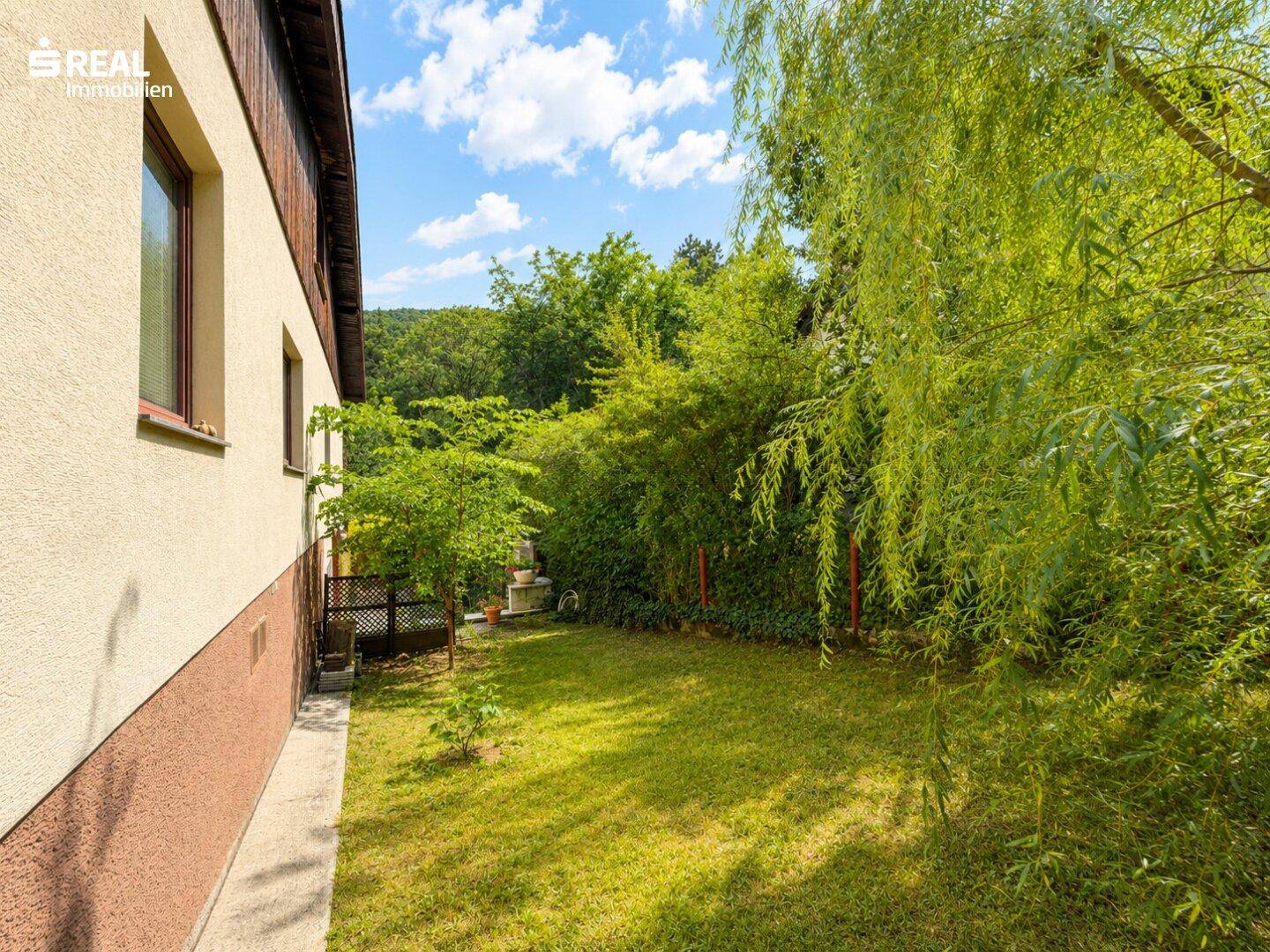Seitenansicht des Hauses mit gepflegtem Rasen und üppigen Bäumen.