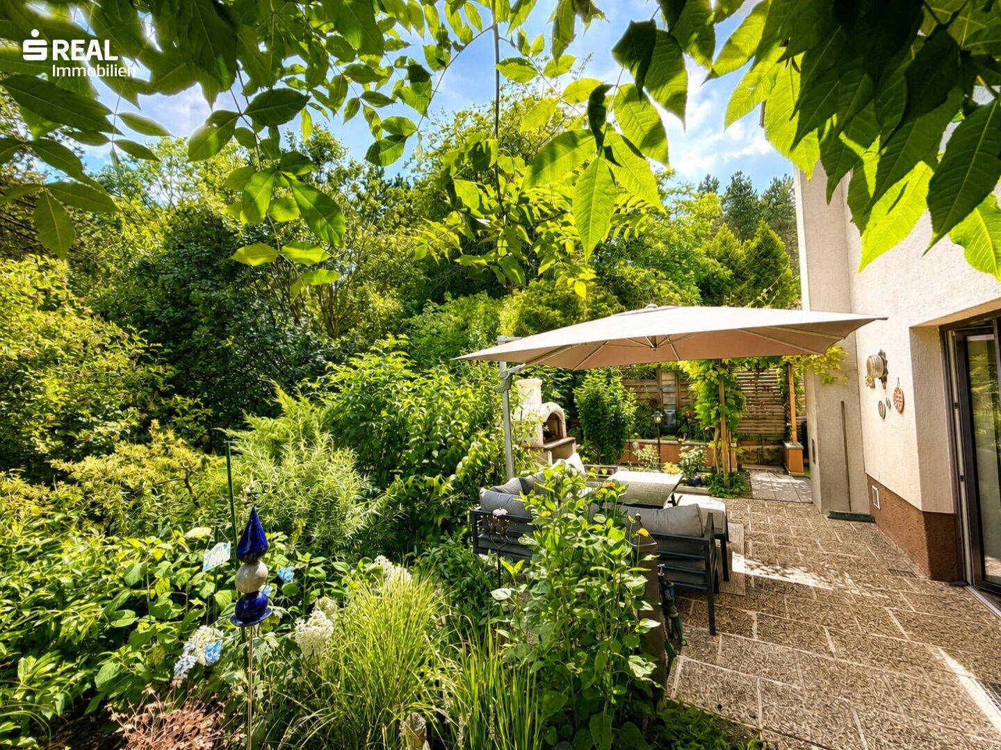 Weitläufige Terrasse umgeben von üppigem Grün und einem gemauerten Ofen für gesellige Abende.