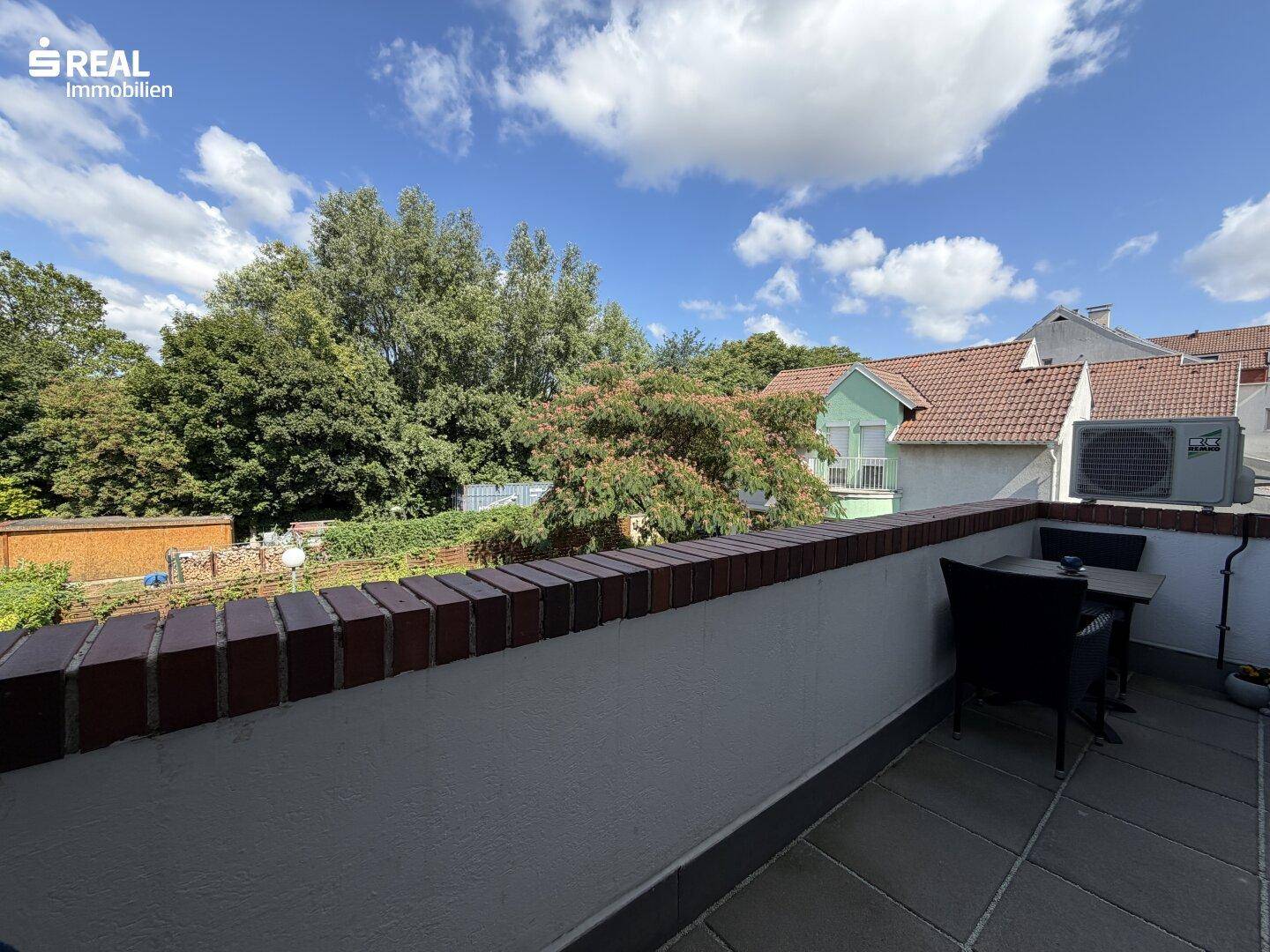 Balkon mit Fliesenboden, Sitzbereich und weitem Blick über die Umgebung.