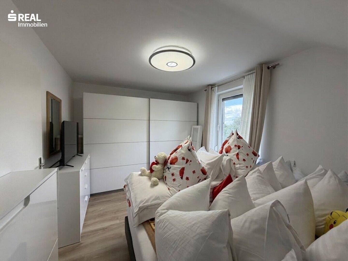 Helles Schlafzimmer mit Bett, Kleiderschrank und Fenster.