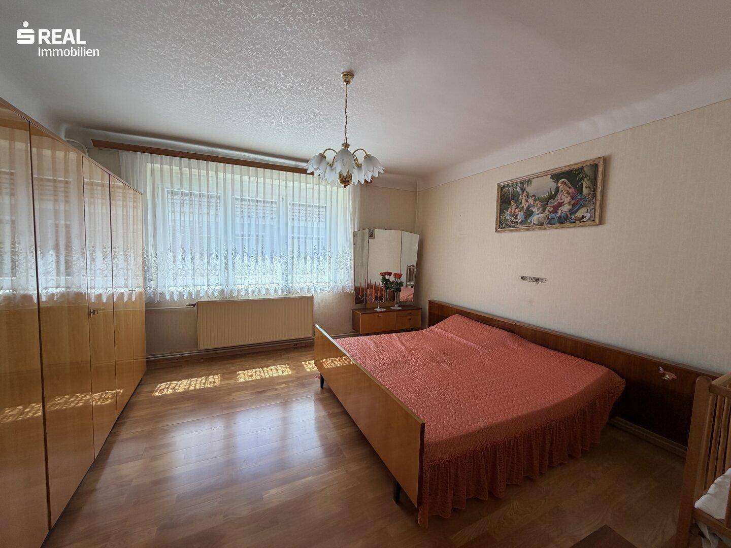 Schlafzimmer mit Holzboden, großem Fenster und traditionellen Holzmöbeln.