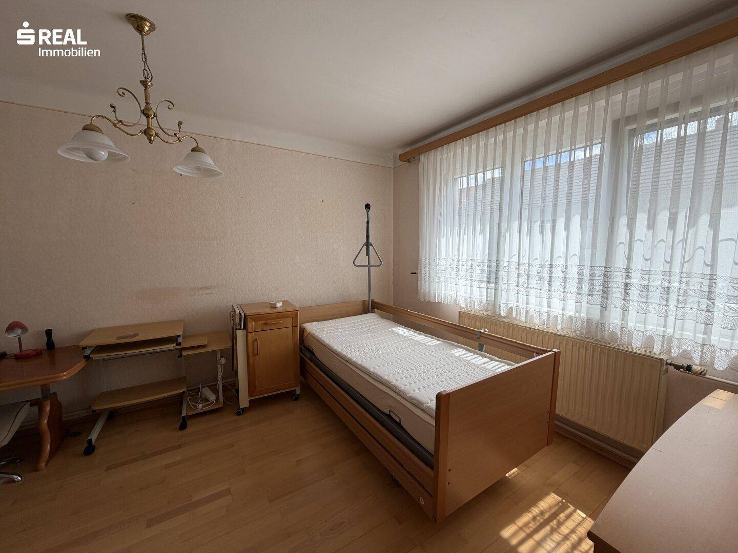 Helles Schlafzimmer mit Einzelbett, Holzboden und großem Fenster.