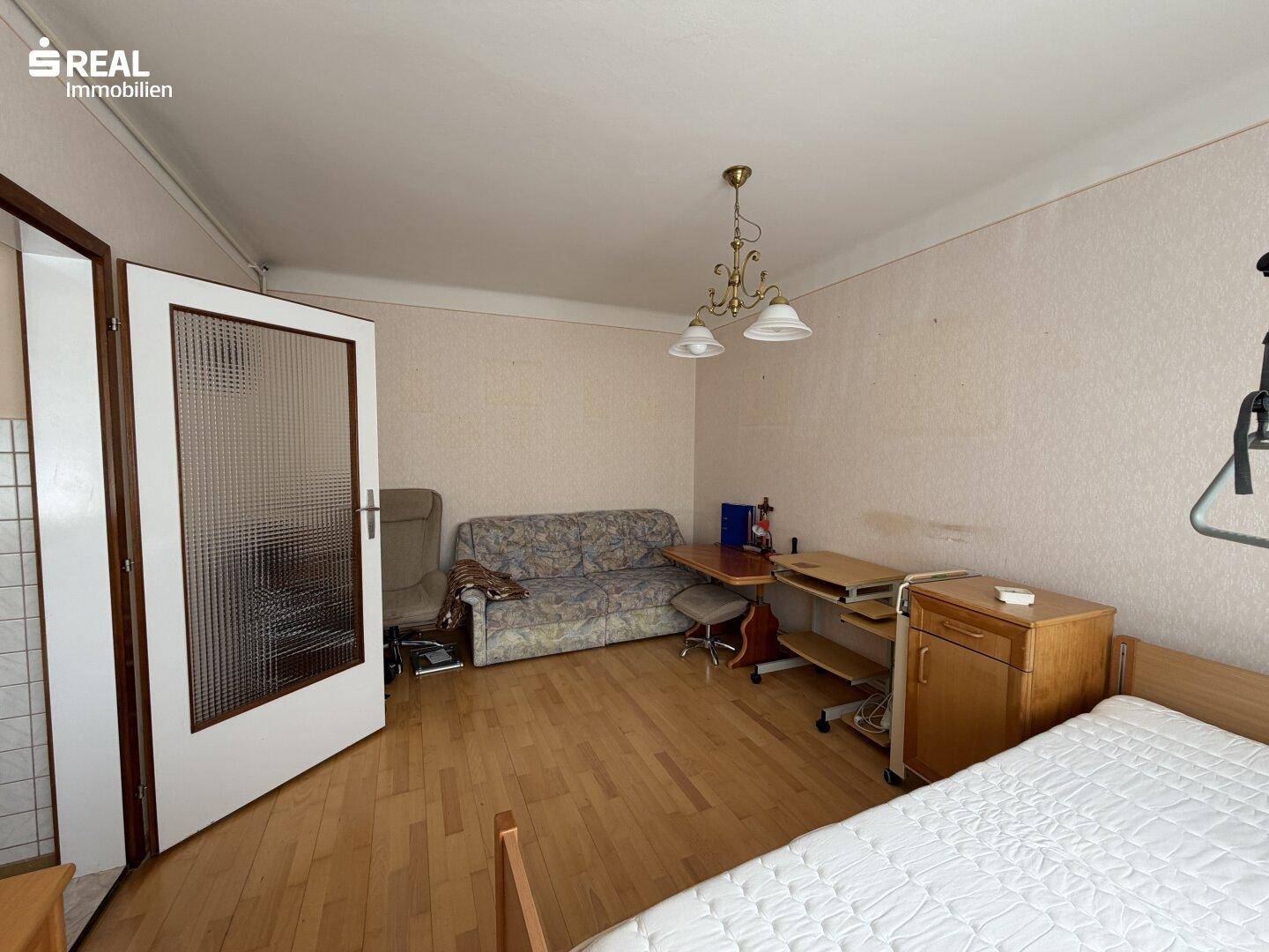 Schlafzimmer mit Holzboden, Sofa und Blick durch eine offene Tür in einen gefliesten Bereich.