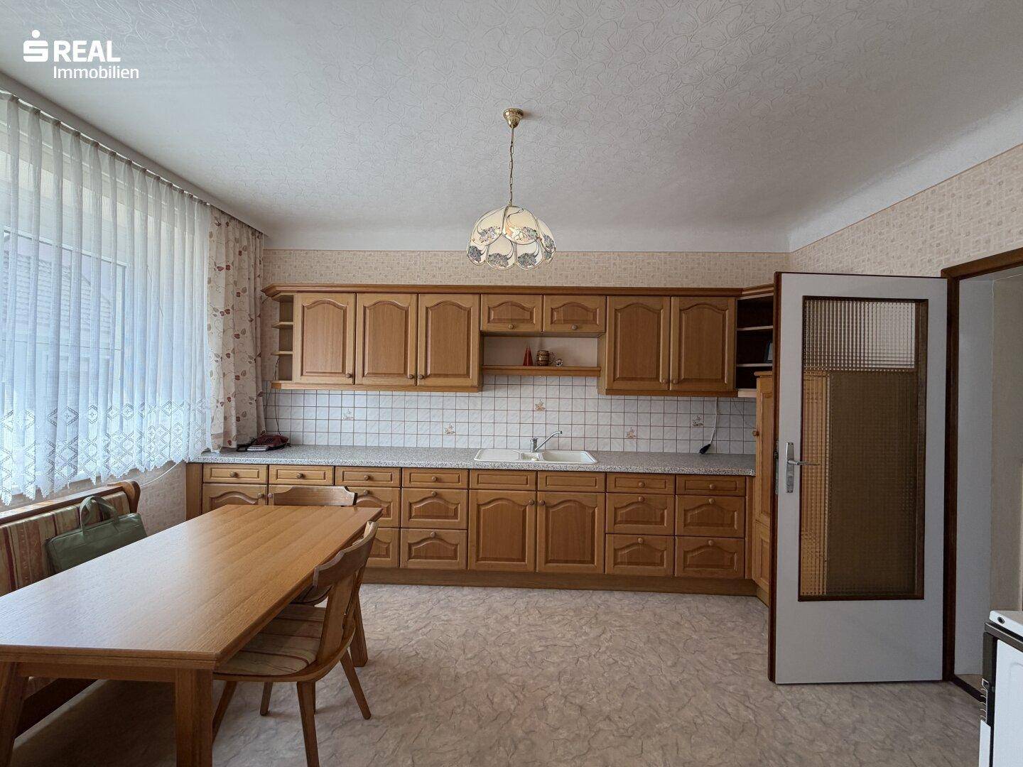 Geräumige Wohnküche mit Holzschränken, Essbereich und Fenster.