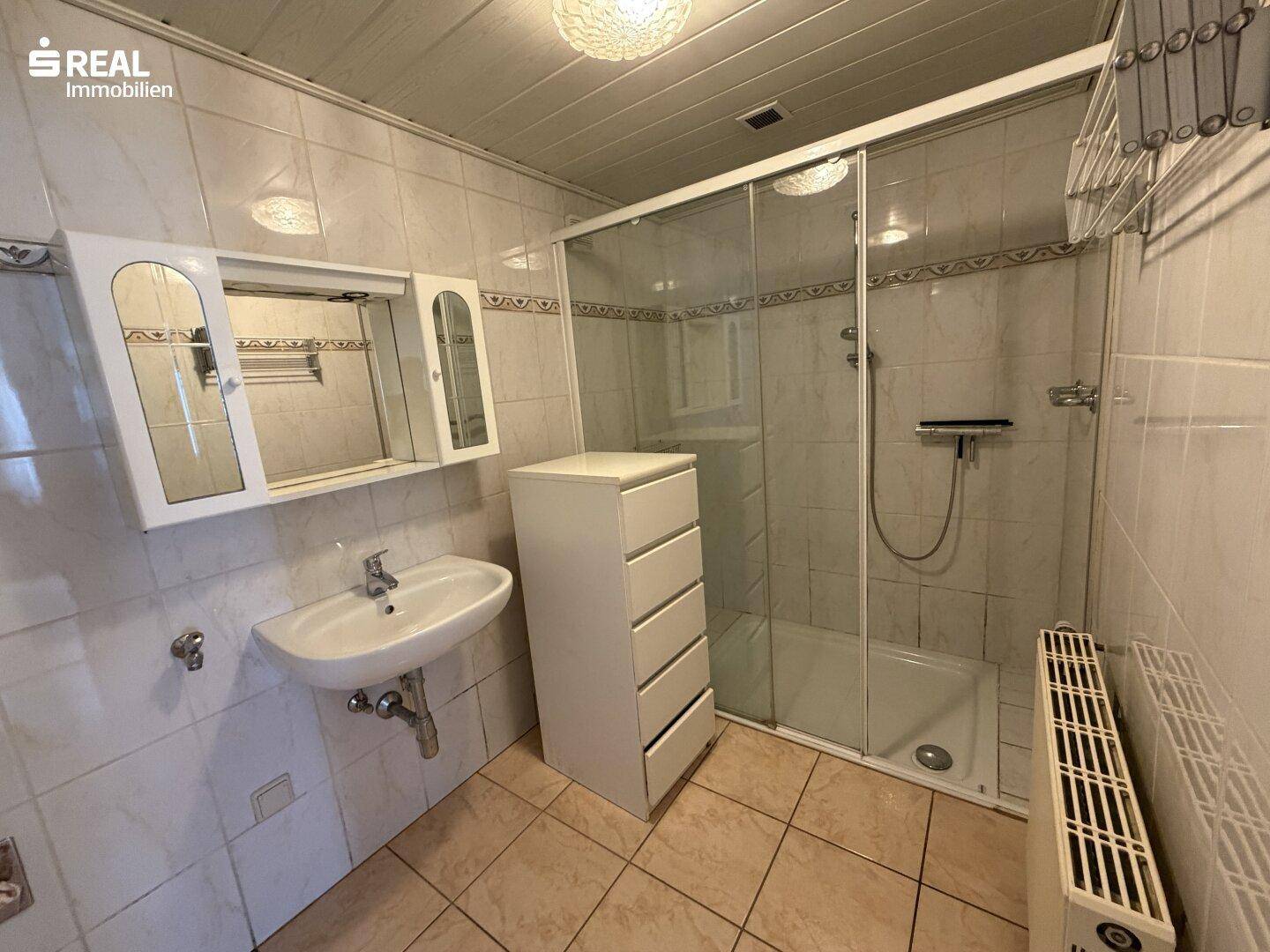 Gefliestes Badezimmer mit Duschkabine, Waschbecken und Spiegelschrank.