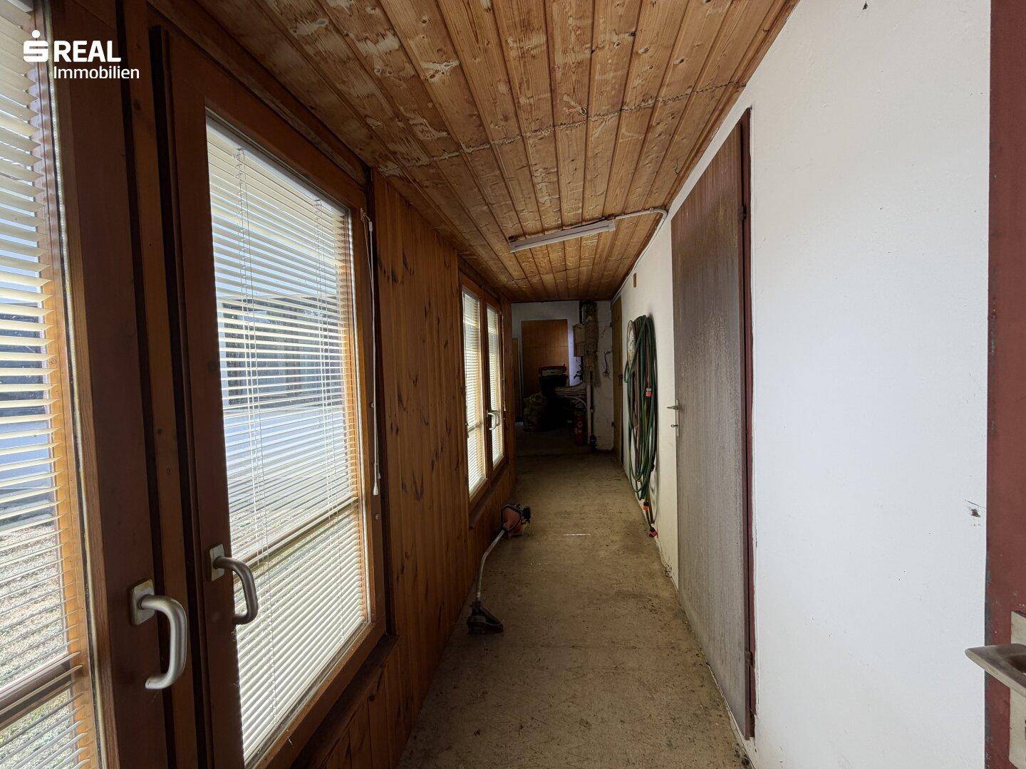 Langer Flur mit Holzdecke, Fenstern und Abstellmöglichkeiten für Gartengeräte.