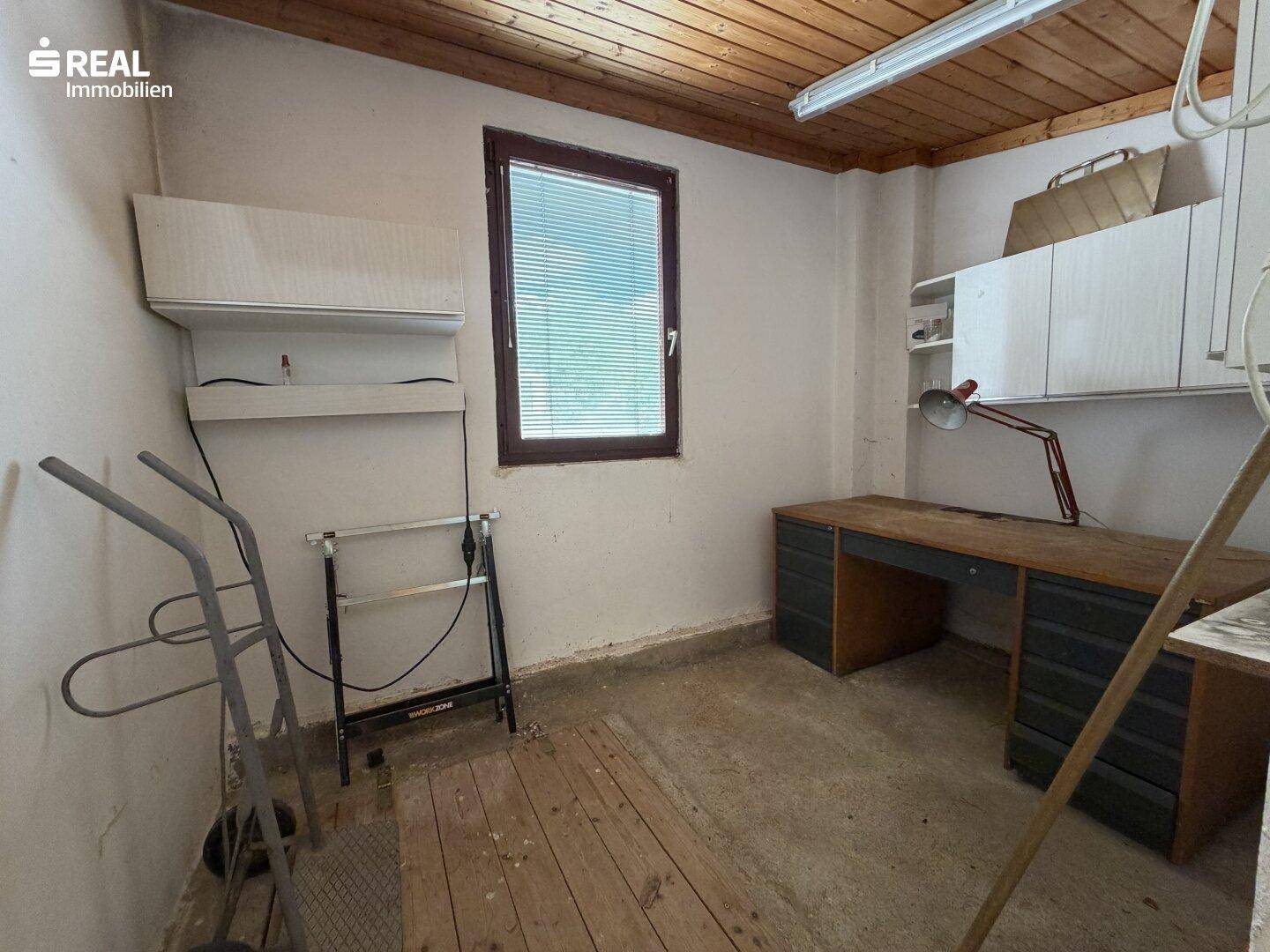 Werkstatt oder Abstellraum mit Holzdecke, Fenster und Arbeitstisch.