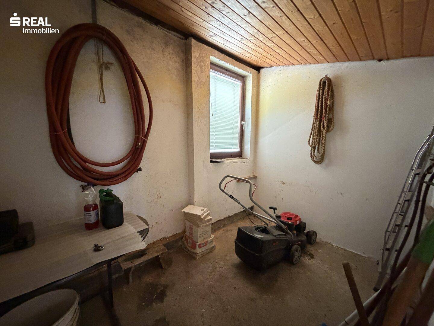 Abstellraum mit Holzdecke, Fenster und verschiedenen Gartengeräten.